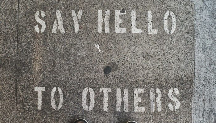 Um chão cinza com a escrita "say hello to others" ou seja, diga "olá" para os outros. A forma Sobre a bondade de Deus